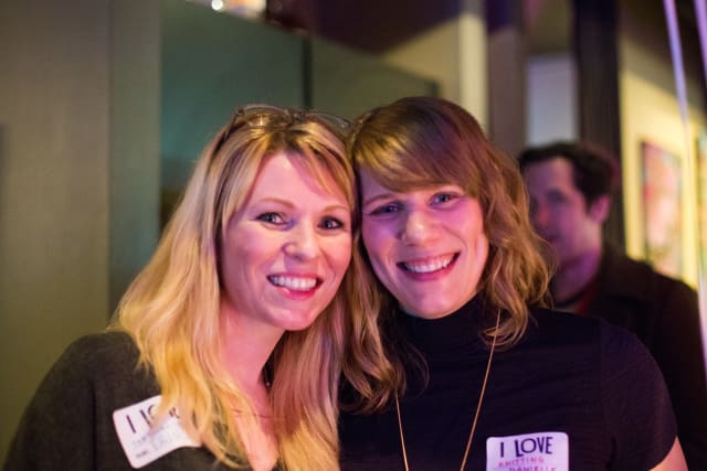 Two smiling women posing together at the Love Bomb 2017 event, wearing name tags, with a vibrant background reflecting a lively atmosphere supporting local youth music education through My Voice Music.